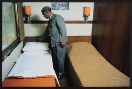 Assistant making bed in railway compartment.