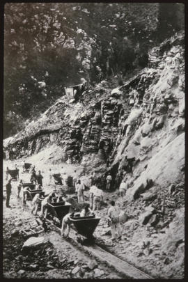 Men removing excavated material in trolleys from large cutting.