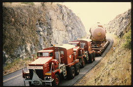 
Two SAR International Pacific trucks with large cylinder on the road through deep cutting.
