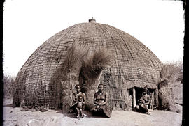Natal. Three Zulu women and baby sitting outside hut.