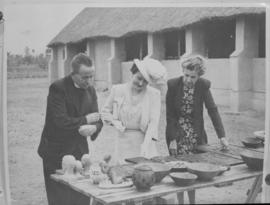 
Queen Elizabeth admiring local craft accompanied by church minister and a woman.
