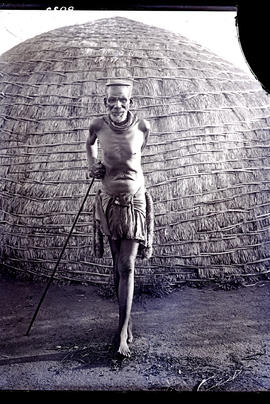 Natal. Old Zulu man leaning on stick in front of hut.