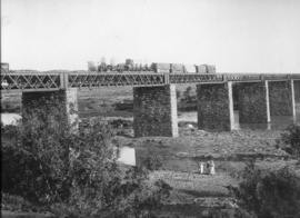 Modder River, 1896. Goods train on bridge over the Modder River with Cape carts on train.