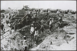 Large manual excavation crew with train in background.