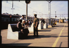 Passengers seated on benches on station platform.