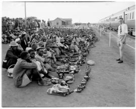 Bechuanaland, 17 April 1947. Crowd with carved and woven goods seated alongside Pilot Train at wa...