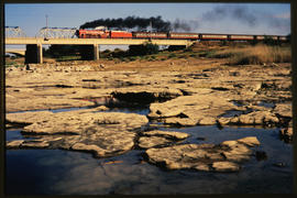 Bloemfontein district, 1976. SAR Class 26 No 3450 'Red Devil' on bridge crossing river with stony...