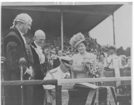 
King George VI signing a book while Queen Elizabeth and bewigged dignitaries look on.  Crowd in ...