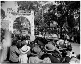 
Royal Family in open car waving to the crowd. Driving through a  'Welcome' sign.
