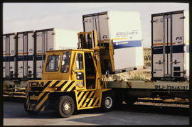 Forklift loading container onto railway wagon.