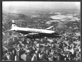Johannesburg. SAA Douglas DC-7B ZS-DKE 'Reiger' in flight over city centre. See N64618. (See C977...