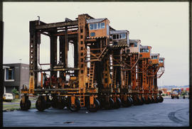 Row of vertical lift straddle carriers for containers.