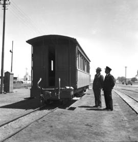 South-West Africa, January 1961. Two men in railway yard observing narrow gauge balcony coach at ...