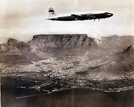 Cape Town, 1963. SAA Douglas DC-7B ZS-DKF 'Good Hope' flying over the city. Table Mountain in the...
