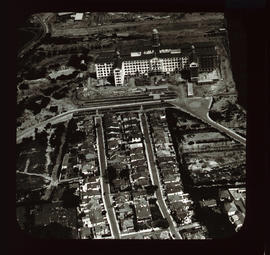Aerial view of large building adjoined by residential houses.