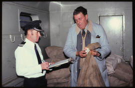 Guard and assistant checking mail bags in mobile post office wagon.