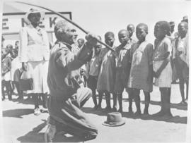 ?Nek' where man is showing children how to use a sjambok?