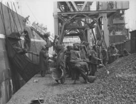Dock workers loading coal onto ship.