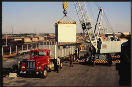 Mobile crane loading container on SAR truck with four-wheeled trailer.