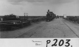 Pokwani, 1895. Stacked rails in the foreground with train hauled by Cape 1st Class in the distanc...