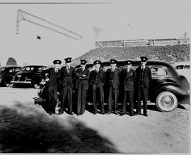 Group of uniformed men at black limousine.