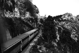 
Goods train entering tunnel with road above.
