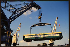 Passenger coach of Hotham Valley Railway lifted by harbour crane from ship in harbour.