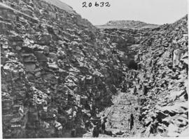 Large rock cutting and tunnel under construction with rock being hauled with trolleys on temporar...