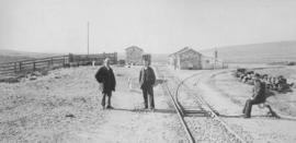 Triangle, 1895. Three railwaymen in the foreground with station buildings in the distance, lookin...