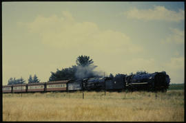 
Two steam locomotives with passenger train in open veld.
