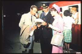 Johannesburg, 1973. Conductor checking passenger list with passengers on station platform.