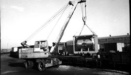 Mobile crane lifting boiler onto train wagon.