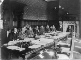 Nine men at boardroom table.