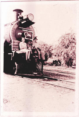 Three people on homemade bench on the front of locomotive.