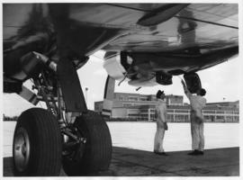 Johannesburg. Technicians inspecting DC-7B aircraft engine from below.