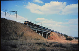 Johannesburg, 1972. 'Trans-Karoo' passenger train headed by SAR Class 6E crossing bridge near Law...