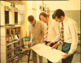 Men consulting drawing in electrical laboratory.