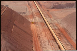 Railway ore wagons and railway tracks runnig between large iron ore stockpiles.