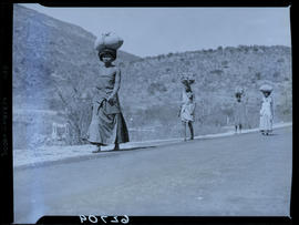 Transkei, 1954. Four women walking in road with bags on heads.