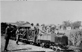 Group of uniformed men with pith helmets at motorised trolley with trailers, probably during the ...