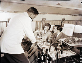 
Dinner being served aboard aircraft. Douglas DC-4 interior. Steward.
