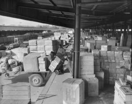 July 1958. Workers loading boxes on trolley at open goods shed.