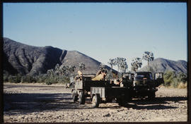 Two trucks with trailers n dry river bed.