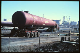 Tubular storage vessel transported in industrial yard.
