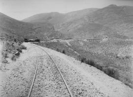 Hex River Mountains, 1895. Steam train approaching bridge with stone piers and seven spans. (EH S...