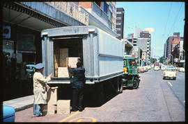 Offloading boxes from a SAR truck in a busy shopping street.