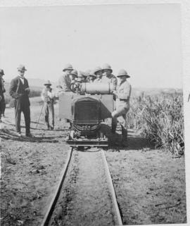 Group of uniformed men with pith helmets at motorised trolley with trailers, probably during the ...