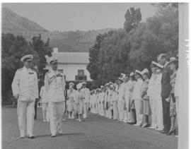 
King George VI and party passing a row of uniformed dignitaries.
