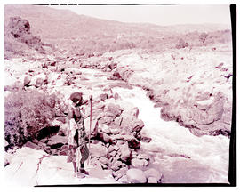 "Nelspruit district, 1962. Man in traditional dress next to river."
