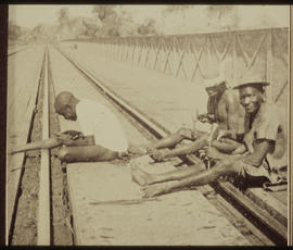 Three men sitting on railway line.